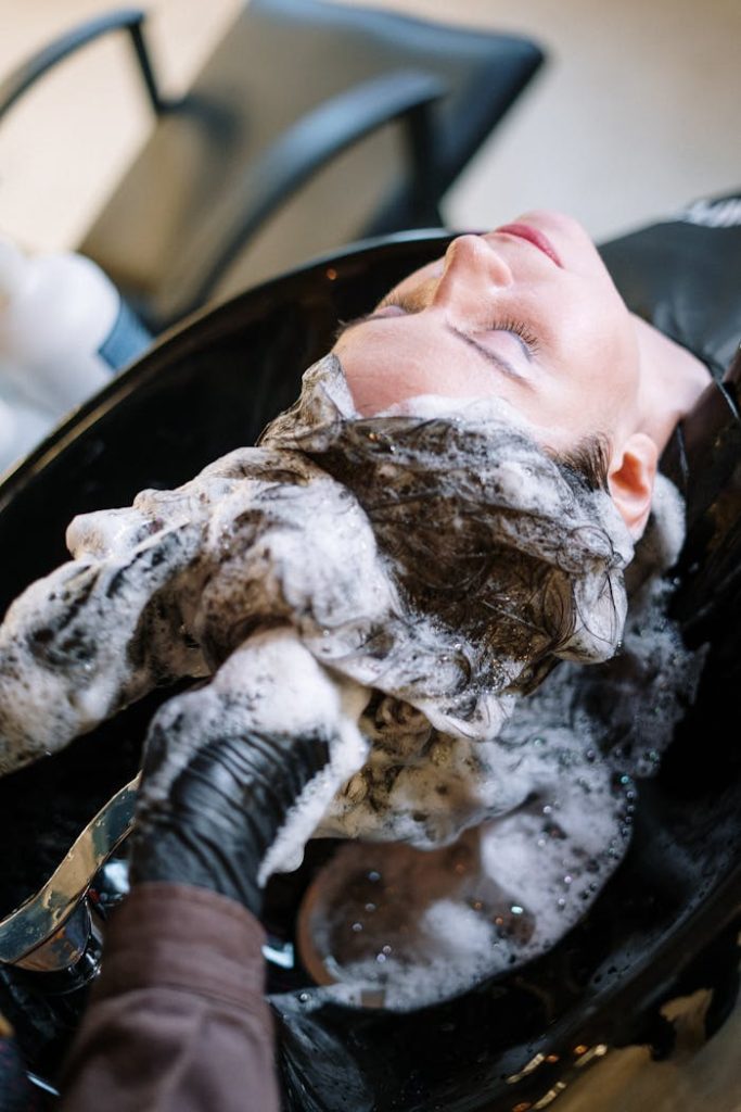 pexels-photo-3993444 A woman getting her hair washed at a salon sink by a professional stylist wearing black gloves.