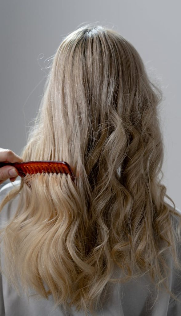 pexels-photo-7440128 Back view of long blonde hair being combed into smooth curls with a red comb.